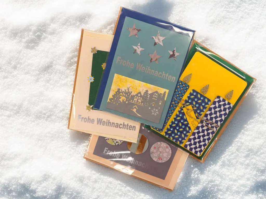 Sortiment handgemachter Weihnachtskarten auf hellem Schnee-Hintergrund.