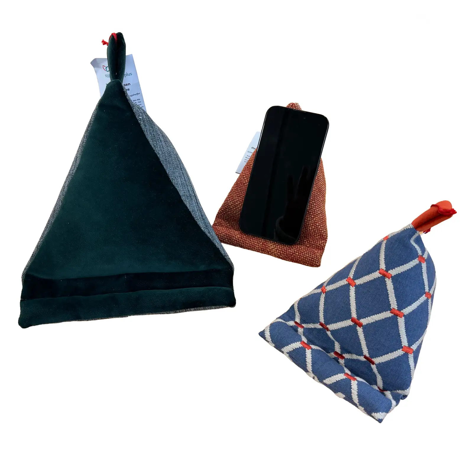 Drei handwerklich gefertigte Tablet- und Handy-Kissen in unterschiedlichen Stoffdesigns, als Gruppe arrangiert. Stiftung 50 Plus.