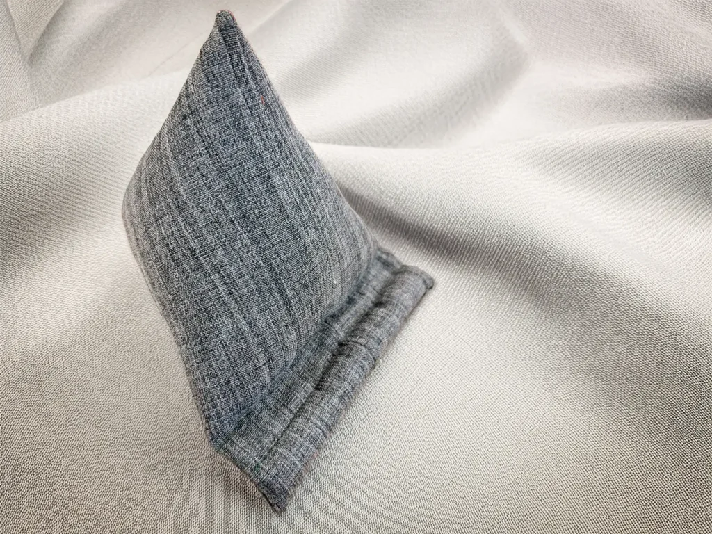 Graues handwerklich gefertigtes Tablet-Kissen auf hellem stoffähnlichem Hintergrund, leicht schräg arrangiert. Stiftung 50 Plus.